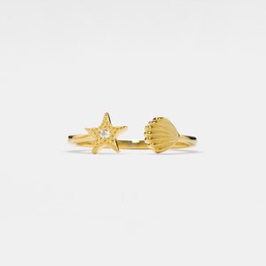 Könnte beinhalten: Goldring mit einem Design aus Seestern und Muschel. Der Seestern hat einen kleinen, klaren Stein in der Mitte.