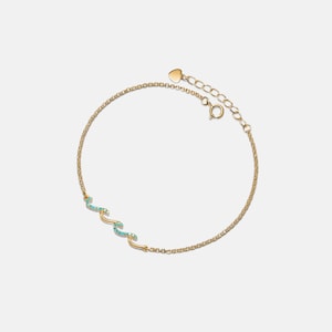 May include: A gold chain bracelet with a turquoise wave charm. The bracelet has a heart-shaped lobster clasp.
