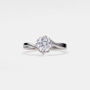 May include: A solitaire engagement ring with a large, round, brilliant-cut diamond. The diamond is set in a prong setting with a swirling, polished silver band. The ring is displayed against a white background.