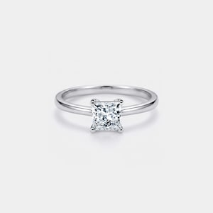 May include: A silver ring featuring a square-cut diamond. The clear, sparkling diamond is set in a simple band. The ring is presented on a white background, emphasising its elegance. The design is classic and timeless.