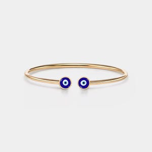 Può includere: Un braccialetto rigido in oro con due ciondoli a forma di occhio blu. I ciondoli hanno un centro bianco e sono posizionati alle estremità del braccialetto.