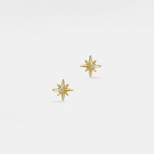 Può includere: Un paio di orecchini a lobo a forma di stella dorata. Ogni orecchino presenta un design a stella con più punte che si irradiano da una gemma centrale e trasparente. Gli orecchini sono su uno sfondo bianco.