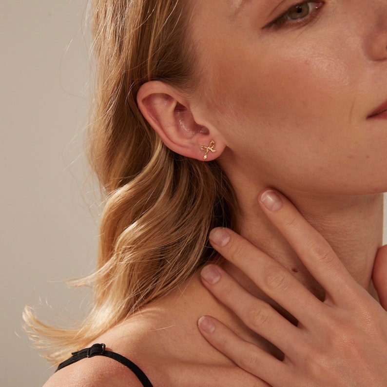 May include: A pair of gold earrings featuring a delicate butterfly design. The earrings are small and simple, making them a perfect everyday accessory.