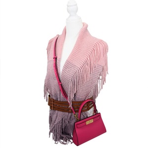 May include: A pink handbag with a gold clasp and a matching pink shoulder strap is displayed on a mannequin. The mannequin is wearing a fringed pink shawl and a brown belt. The shawl has a gradient effect, transitioning from light pink to a darker shade.
