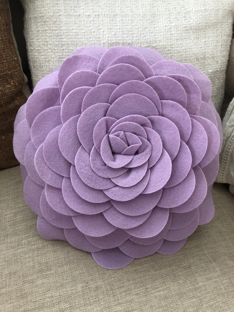 K&ouml;nnte beinhalten: Ein gro&szlig;es, rundes, lilafarbenes Kissen in Blumenform. Das Kissen ist aus weichem, pl&uuml;schem Stoff gefertigt und hat ein 3D-Design.