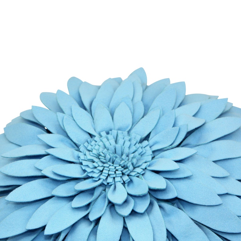 May include: A light blue decorative pillow with a flower design. The pillow features layered petals in a soft, pastel blue color, creating a three-dimensional floral effect. The center of the flower has a textured, fringed appearance.