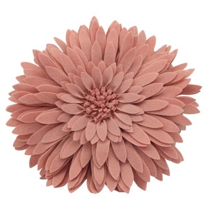 May include: A round, dusty rose-colored decorative pillow shaped like a large flower. The pillow features layered, petal-like felt pieces radiating from the center, creating a three-dimensional floral design. The pillow is a soft, muted pink.