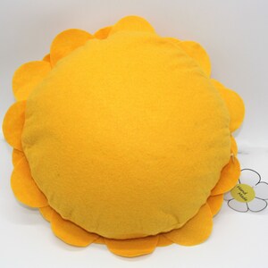 K&ouml;nnte beinhalten: Ein rundes gelbes Kissen mit einem blumenf&ouml;rmigen Rand. Das Kissen hat ein wei&szlig;es Etikett mit der Aufschrift "Hand Made".