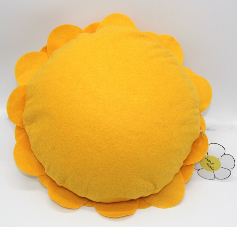 K&ouml;nnte beinhalten: Ein rundes gelbes Kissen mit einem blumenf&ouml;rmigen Rand. Das Kissen hat ein wei&szlig;es Etikett mit der Aufschrift "Hand Made".