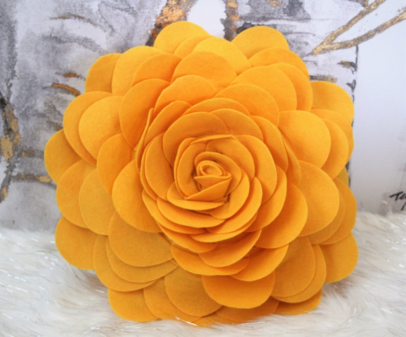 K&ouml;nnte beinhalten: Ein gro&szlig;es, gelbes Filzblumenkissen. Die Blume besteht aus vielen &uuml;berlappenden Bl&uuml;tenbl&auml;ttern, die einen 3D-Effekt erzeugen.