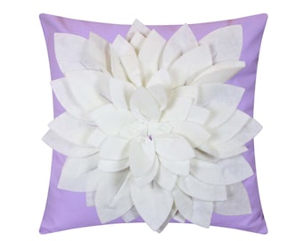 May include: A lavender square pillow with a large white felt flower in the center. The flower has many petals and is raised from the pillow.