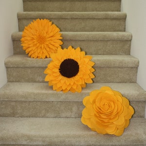 K&ouml;nnte beinhalten: Drei gro&szlig;e gelbe Filzblumen-Dekorationen auf einer mit Teppich ausgelegten Treppe. Die Blumen haben die Form von Sonnenblumen und Rosen.