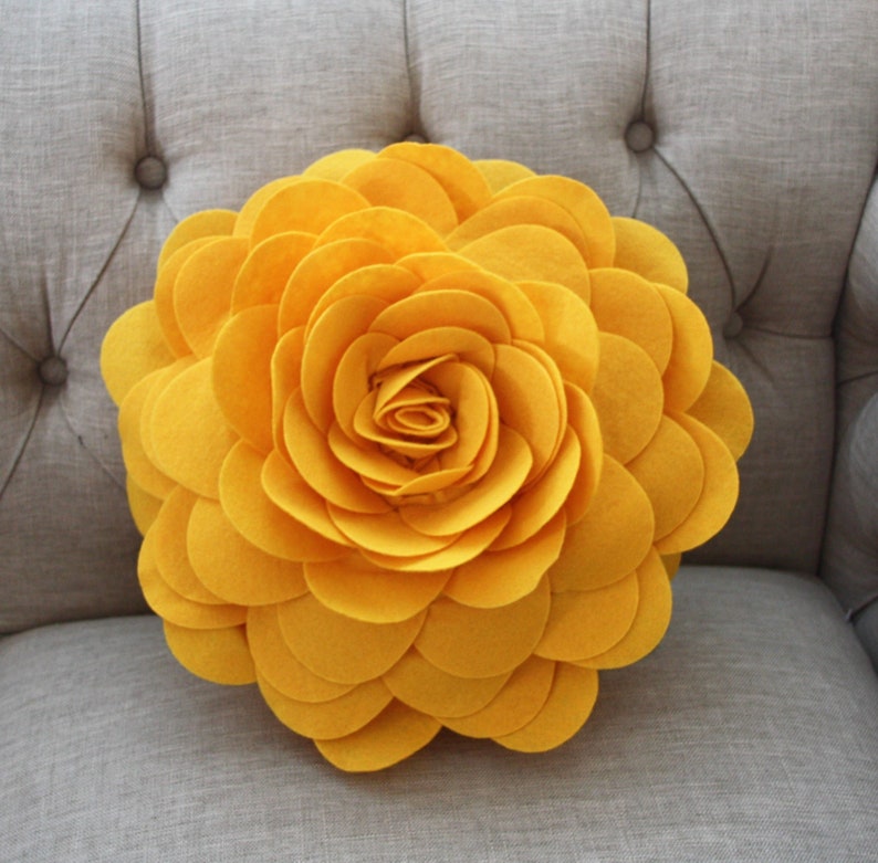 K&ouml;nnte beinhalten: Ein gro&szlig;es, gelbes Kissen in Form einer Blume aus Filz. Das Kissen besteht aus vielen Schichten von Filzbl&uuml;tenbl&auml;ttern, die einen 3D-Effekt erzeugen.