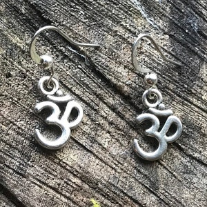 May include: A pair of silver Om symbol earrings. The earrings are small and delicate, with a simple design. They are perfect for everyday wear or for special occasions.