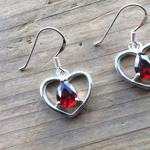 May include: A pair of silver heart-shaped earrings with a red gemstone in the center of each heart.