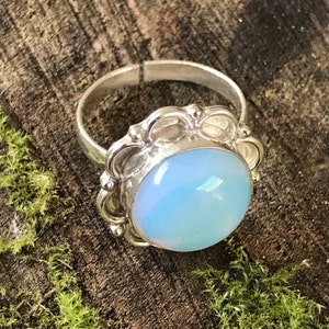 Puede incluir: Un anillo de plata con una piedra de ópalo azul claro engastada en un diseño floral decorativo.