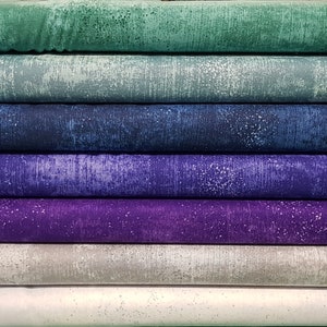 May include: A stack of fabric in various shades of blue, green, and purple. The fabric has a textured, speckled appearance, with a distressed or weathered look. The colors range from light teal to deep indigo and violet.