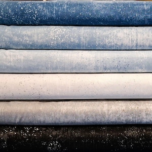 May include: A stack of fabric rolls in varying shades of blue, gray, and white. Each roll has a textured, speckled appearance, with the colors ranging from deep indigo to a light, almost pearly white. The fabric appears to be tightly woven.