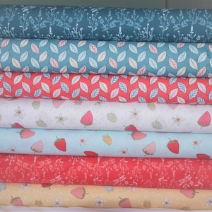 May include: A stack of eight fabric rolls featuring various patterns. The designs include a blue floral print, a blue and pink leaf pattern, a red and pink leaf pattern, a white background with red strawberries and white flowers, a light blue background with red strawberries and white flowers, a red background with white floral sprigs, a yellow background with red strawberries and white flowers, and a white background with a blue floral design.