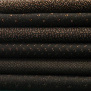 May include: A stack of five fabric rolls featuring various patterns in brown and black. The designs include small floral motifs, geometric shapes, and swirls.