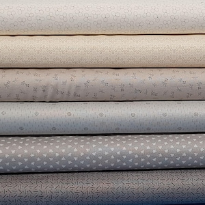 May include: A stack of fabric rolls in various neutral tones. Each roll displays a different pattern, including floral, geometric, and abstract designs. The fabrics range in color from cream to gray, offering a variety of textures and visual interest.