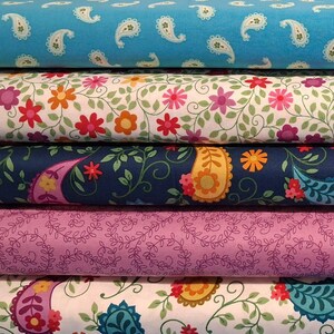May include: A stack of fabric rolls with various floral and paisley patterns. The top roll is light blue with white paisley designs. Other rolls feature floral and paisley patterns in pink, orange, green, and purple on white, navy, and lavender backgrounds.