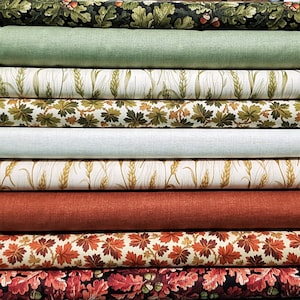 May include: A stack of ten fabric swatches featuring various autumnal patterns. The swatches include designs of leaves, acorns, wheat, and floral patterns in shades of green, brown, red, and cream.