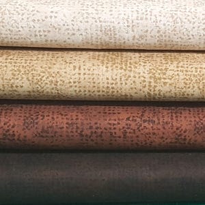 May include: Four fabric swatches stacked on top of each other. The top swatch is a light beige with a subtle speckled pattern. The second swatch is a light brown with a speckled pattern. The third swatch is a dark brown with a speckled pattern. The bottom swatch is a dark brown with a smooth texture.