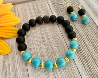 Pode incluir: Um bracelete de contas pretas e turquesa com detalhes dourados e brincos combinando. O bracelete apresenta contas de lava preta e contas turquesa com detalhes dourados. Os brincos são feitos de contas pretas com detalhes turquesa e ganchos dourados.
