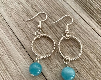 Puede incluir: Un par de pendientes de aro de plata con una piedra preciosa azul claro colgando de cada aro.