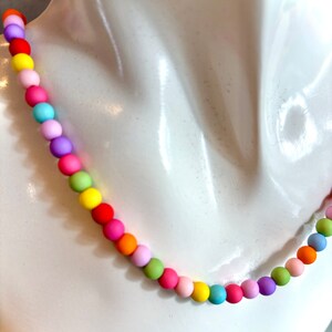 May include: A colorful rainbow beaded necklace with round, matte beads in various shades of pink, yellow, green, blue, and orange.
