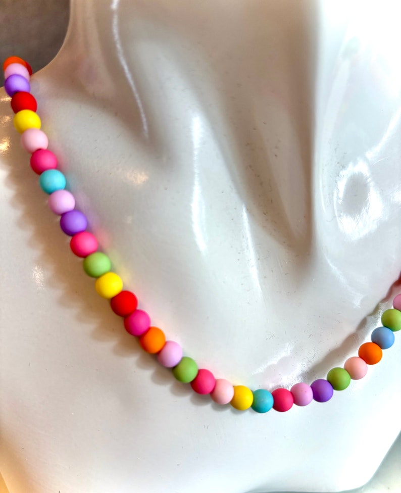 May include: A colorful rainbow beaded necklace with round, matte beads in various shades of pink, yellow, green, blue, and orange.
