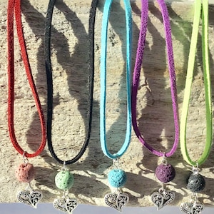 May include: Six lava stone necklaces with silver heart charms. The necklaces are on a wooden background and come in red, black, turquoise, purple, green, and black.