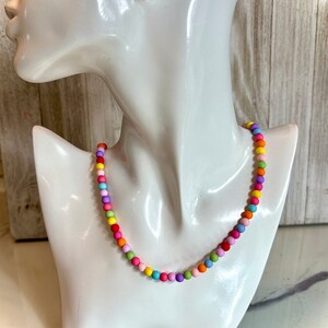 May include: A colorful beaded necklace with a rainbow of colors, including pink, purple, blue, green, yellow, and orange. The necklace is on a white mannequin.