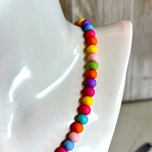 May include: A colorful beaded necklace with round beads in shades of pink, orange, yellow, green, blue, and purple.