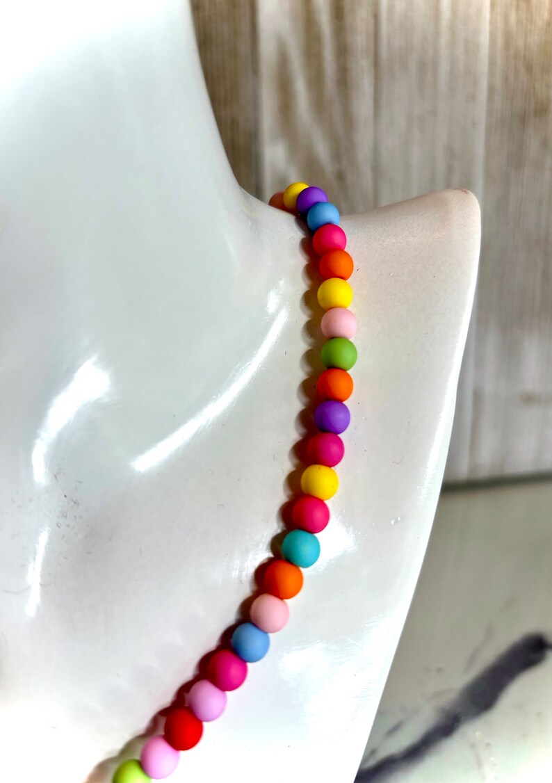 May include: A colorful beaded necklace with round beads in shades of pink, orange, yellow, green, blue, and purple.