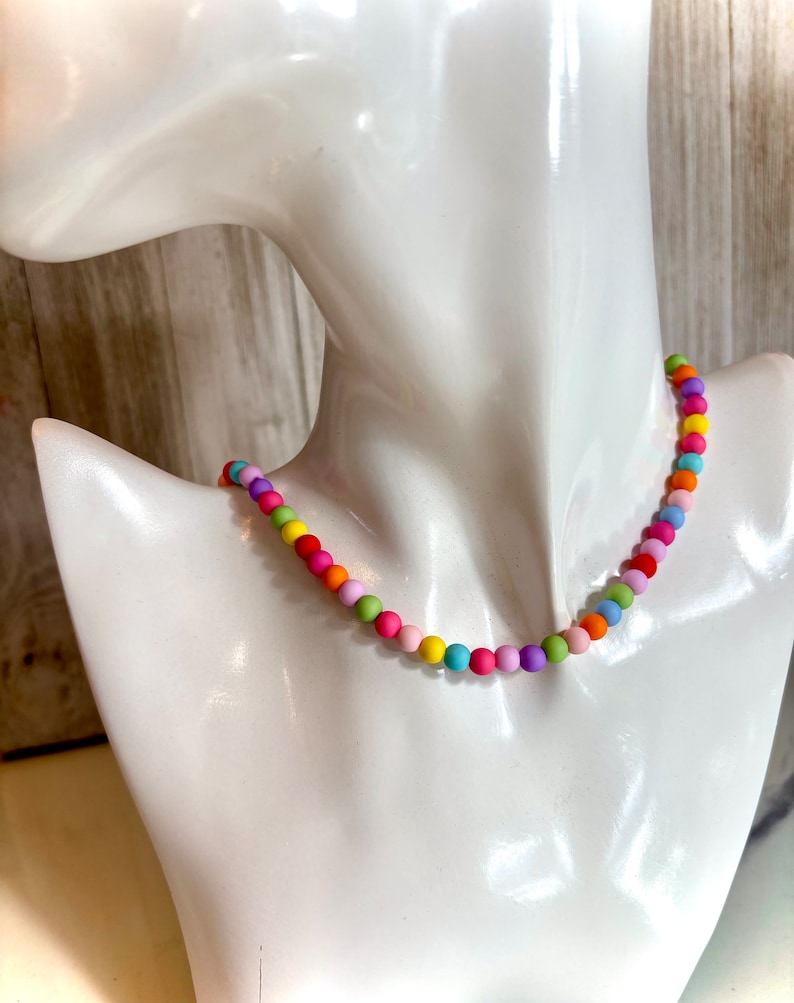 May include: A colorful beaded necklace with alternating pastel colors, including pink, purple, yellow, green, and orange.