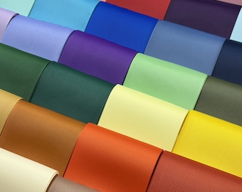 May include: A collection of grosgrain ribbon rolls arranged in a grid pattern, featuring a diverse spectrum of solid colors including shades of red, blue, green, yellow, orange, purple, pink, brown, and cream with a distinct ribbed texture.