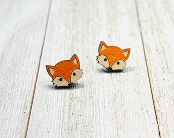 May include: A pair of fox-shaped wooden earrings. The earrings are orange with black eyes and a black nose.