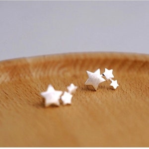 May include: Two pairs of silver star stud earrings. Each pair has three stars of varying sizes.