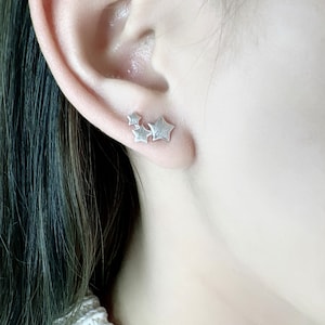 May include: A close-up of a silver star-shaped earring with three stars clustered together.