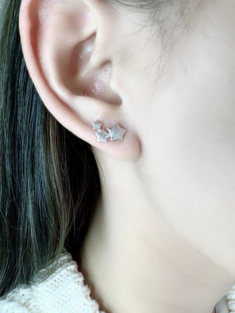 May include: A close-up of a silver star-shaped earring with three stars clustered together.