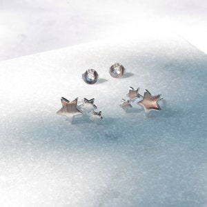 May include: Two silver star shaped earrings. Each earring has three stars of different sizes. The stars are clustered together.