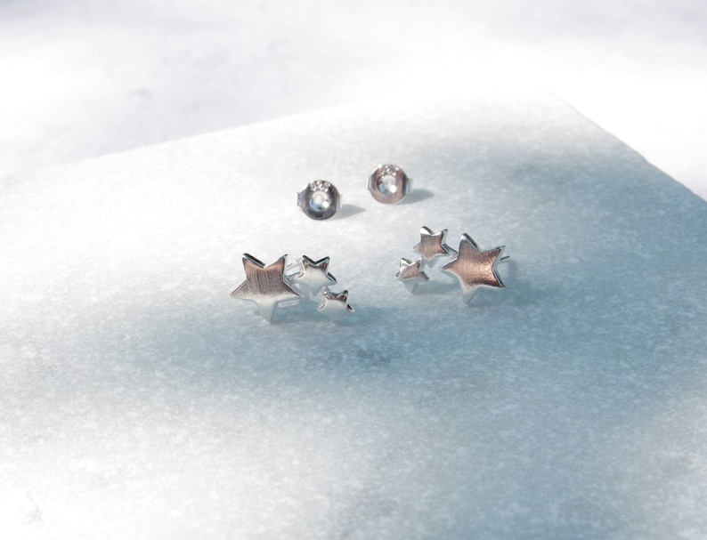 May include: Two silver star shaped earrings. Each earring has three stars of different sizes. The stars are clustered together.