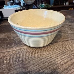 Puede incluir: Cuenco mezclador de cerámica color crema con rayas azules y granates. El cuenco tiene un exterior acanalado y un borde ancho y ligeramente ensanchado. Un artículo de cocina vintage.