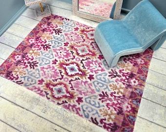 May include: Miniature dollhouse interior scene featuring a patterned rug in shades of pink, purple, and blue. A light blue chair, a decorative mirror, and a small lamp are also visible. The rug measures approximately 12 inches by 8 inches.