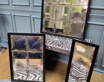 May include: Three decorative mirrors with black frames. The mirrors are divided into smaller squares, creating a unique, antique look. The mirrors are placed on a zebra-print rug and a patterned surface, adding visual interest.
