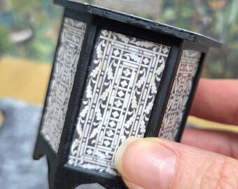 May include: A miniature black and white patterned cabinet with a rectangular shape. The cabinet has a black frame and a decorative, repeating pattern on the sides. The cabinet is a small scale model.