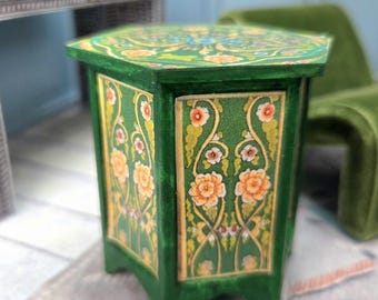 May include: A small, green wooden side table with floral designs. The table has a hexagonal top and is painted with orange and yellow flowers and gold accents. The table is a decorative piece.