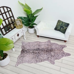 May include: A pink and brown cowhide rug with a leopard print pattern. The rug is in a living room setting with a white sofa and a potted plant.